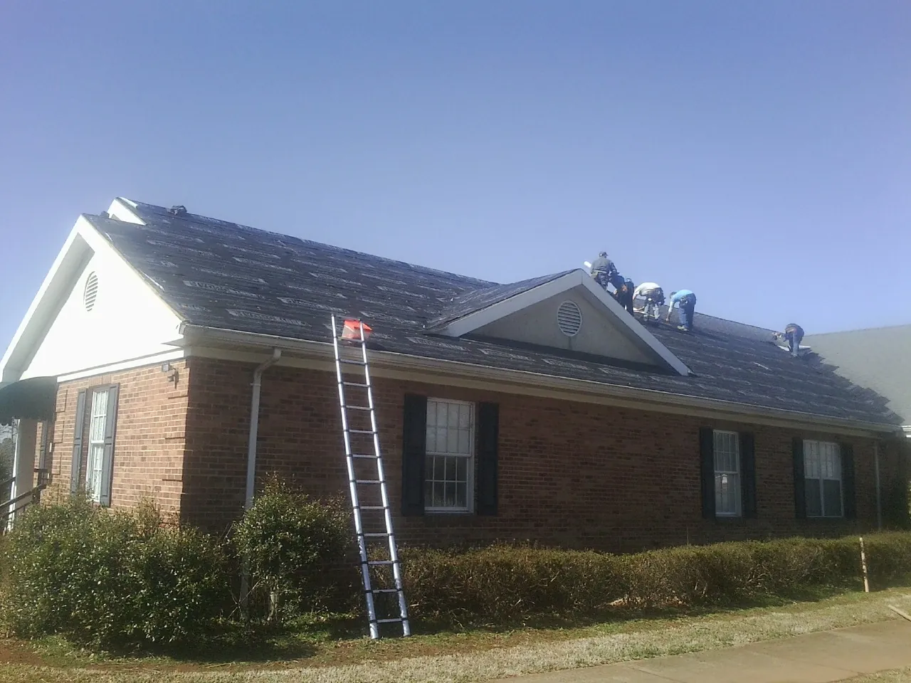 Crew tearing shingles off a brick ranch roof with a ladder set — Emergency Roof Repair work by our crew in Foothill Ranch