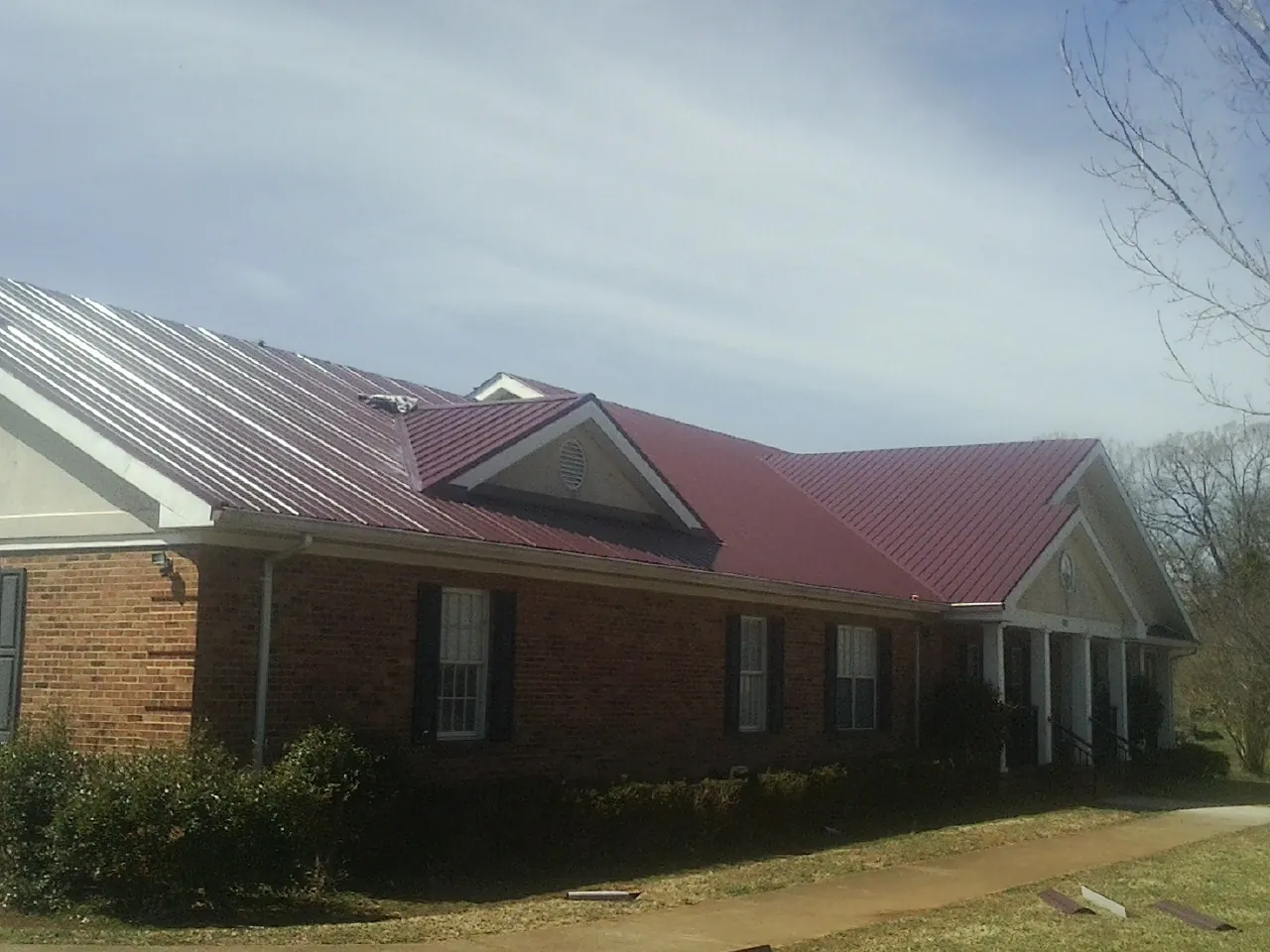 Red metal roof with gabled entries on a long brick building, from a Hail Damage Roof Repair job in Foothill Ranch