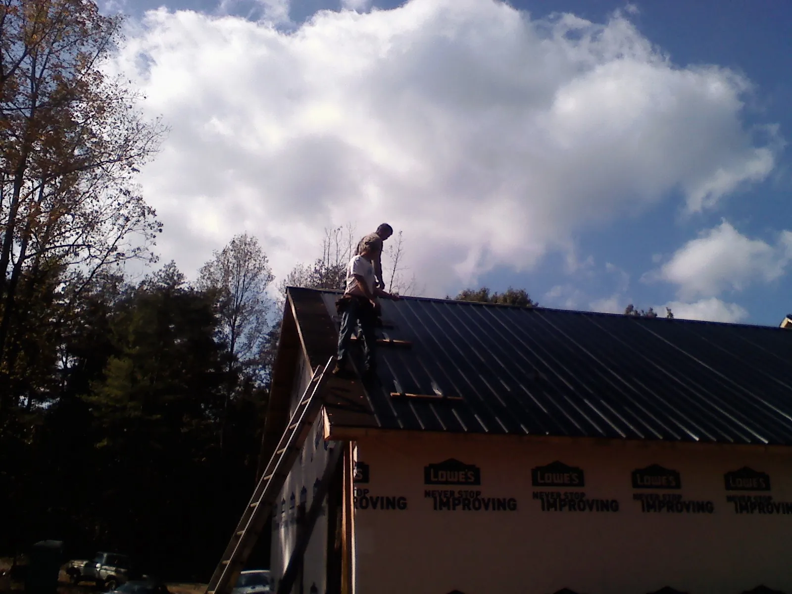 Roofer fastening dark metal panels high against a cloudy sky, from a Roof Inspection job in Foothill Ranch